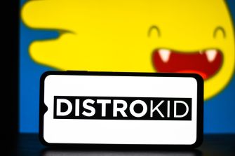 DistroKid logo displayed on a sign in front of a smiling yellow cartoon face.