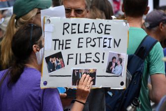 Protesters hold a sign reading “Release the Epstein Files!” with photos attached.