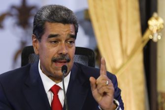 Nicolás Maduro speaks into a microphone and raises one finger during a formal event.