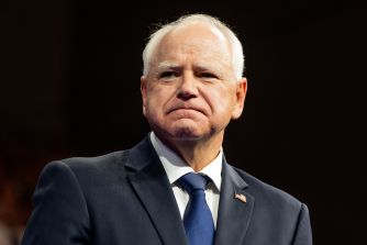 Minnesota Gov. Tim Walz stands in a suit and tie with a serious expression.