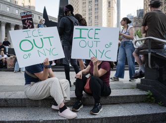 Protesters sit on city steps holding signs reading “ICE OUT OF NYC” during an immigration demonstration.