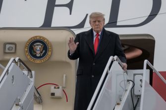 President Donald Trump waves while descending the stairs of a U.S. government aircraft.