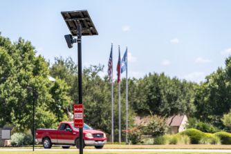 Solar-powered license plate camera overlooking a road with a red pickup truck and American flags in the background.