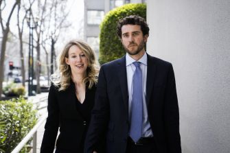 Elizabeth Holmes and Billy Evans walk together outdoors beside a building.