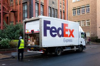 FedEx Express delivery truck parked outside a brick building as a worker unloads packages.