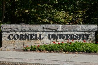 Cornell University stone entrance sign surrounded by trees and red flowers.