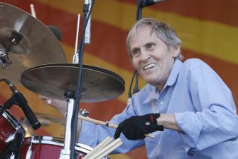 Levon Helm smiles while playing drums onstage.