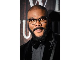 Tyler Perry poses in a black tuxedo and glasses at an event.