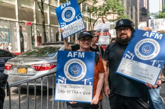 Musicians protest outside a city street holding AFM signs calling for support of a new sound recording labor agreement and consent, credit and compensation for AI use.