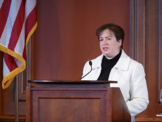 Elena Kagan speaks at a lectern in front of an American flag.