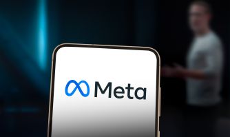 Meta logo displayed on a smartphone, with a blurred person standing in the background.