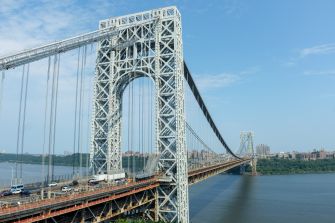 George Washington Bridge spanning the Hudson River, with traffic crossing its lower roadway beneath a clear blue sky.