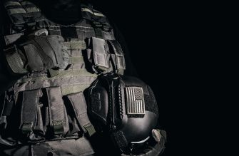 Tactical body armor vest with pouches, a radio, and an American flag patch against a black background.