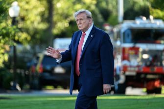 Donald Trump gestures while walking on a lawn, with a fire truck in the background.