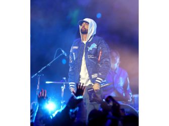 Eminem performs onstage in a hooded jacket as audience members raise their hands.