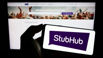 Silhouette holding a StubHub logo card in front of a computer displaying the StubHub website.