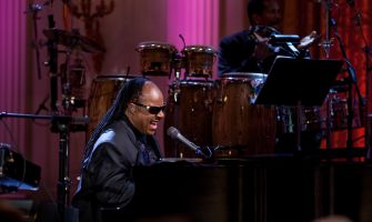 Stevie Wonder sings and plays piano onstage during a performance.