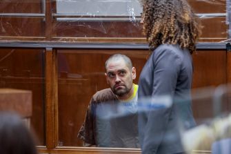 Nick Reiner sits in a courtroom behind a glass partition as an attorney stands in the foreground.