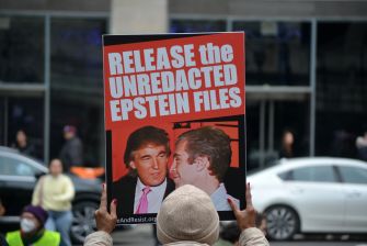 Person holds a sign reading “Release the Unredacted Epstein Files” featuring Donald Trump and Jeffrey Epstein.
