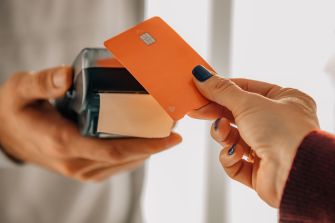 Person paying with an orange debit card at a handheld card reader.