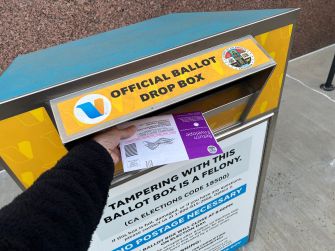 A voter places a mail-in ballot into an official ballot drop box.