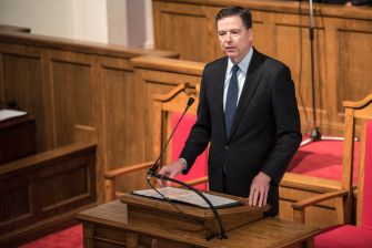 Former FBI Director James Comey speaks at a wooden lectern in a courtroom.