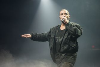 Aubrey Drake Graham performs onstage under a spotlight, holding a microphone and extending one arm.