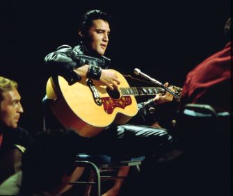 Elvis Presley plays an acoustic guitar during a performance.