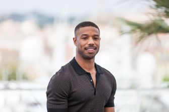 Michael B. Jordan poses outdoors in a black short-sleeved shirt.