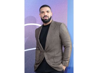Drake poses in a brown checked blazer at a public appearance.