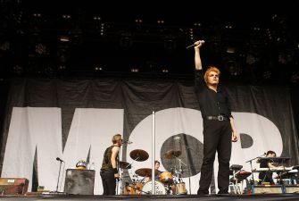 My Chemical Romance vocalist holds a microphone overhead onstage with the band performing behind him.
