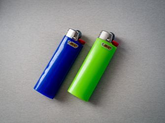 Two BIC pocket lighters, one blue and one green, lie side by side on a gray surface.