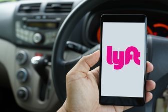 Hand holding a smartphone displaying the Lyft logo inside a car.