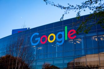 Google logo on the glass facade of an office building under a clear blue sky.