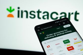Instacart logo behind a smartphone displaying the company’s grocery delivery and pickup app.