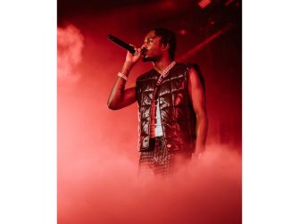 Male rapper performing on stage with a microphone, red lighting and smoky haze in the background.