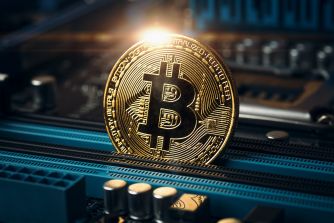 Close-up of a gold Bitcoin coin resting on a blue computer motherboard, symbolizing cryptocurrency.
