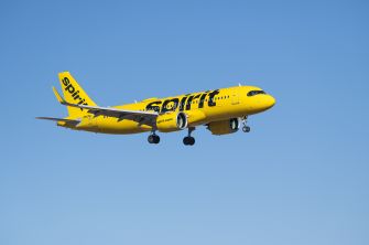 Yellow Spirit Airlines plane in mid-flight against a clear blue sky.