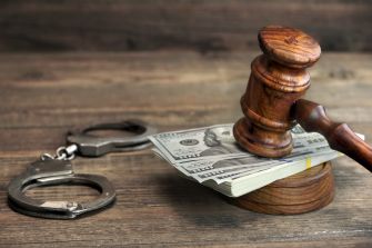 A gavel resting on a stack of cash with handcuffs nearby, symbolizing bail reform and the justice system.