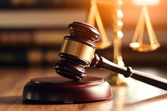 A wooden gavel placed on a sounding block with a blurred background of legal scales and books, symbolizing justice and legal proceedings.