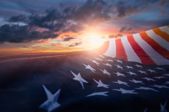 A US flag gently waving in the wind with a sunset backdrop.