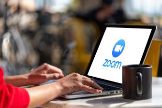 A person using a laptop with the Zoom logo on the screen, accompanied by a coffee mug.