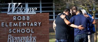 A group of individuals mourning together near the sign of Robb Elementary School in Uvalde, Texas.