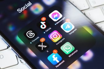 Close-up of a smartphone screen with a folder labeled Social, displaying app icons for TikTok, Instagram, Threads, Facebook, WhatsApp, Telegram, Messenger, and X (Twitter).