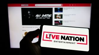 Close-up of a hand holding a tablet displaying a large Live Nation Entertainment sign, in front of a computer monitor showing a Live Nation page.