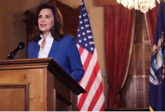 Michigan Governor Gretchen Whitmer speaking at a podium in front of the state flag and a U.S. flag after signing new sex offender amendments into law.