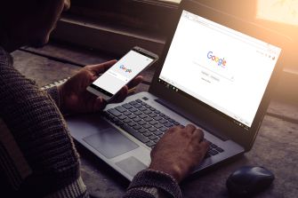 A person using a smartphone and laptop to access the Google search engine.
