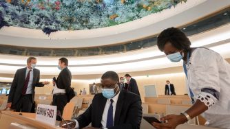A meeting setting in a United Nations conference room, with delegates wearing masks, engaged in discussion.