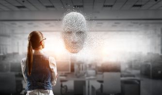 A person standing in an office environment, looking at a digital representation of a human face made up of particles and light.