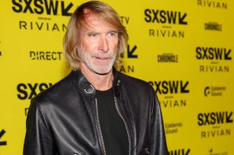 Portrait of a man with shoulder-length blond hair wearing a black leather jacket, standing against a yellow SXSW backdrop.